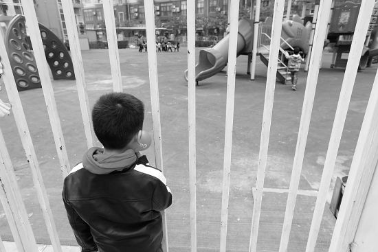 一名受影响的小孩在幼儿园外看着小伙伴玩耍 摄/法制晚报记者黑克